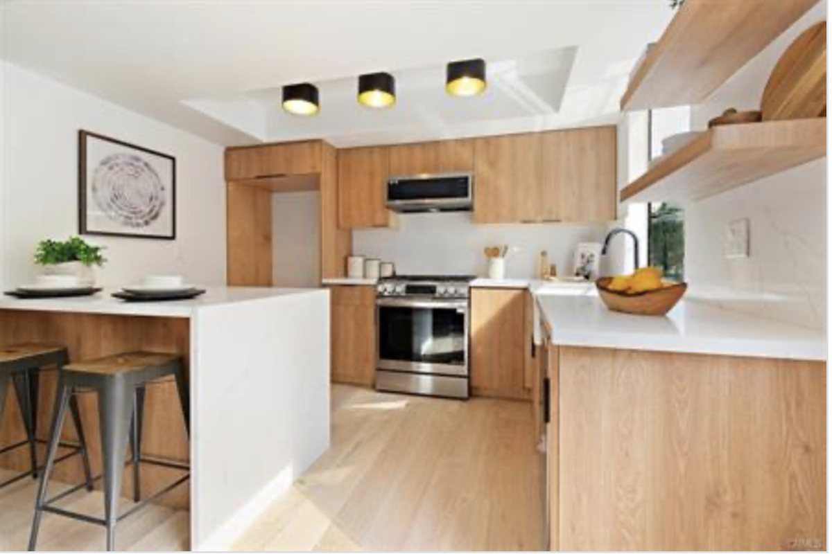 Renovated kitchen after — light cabinetry, waterfall quartz island, and open shelving